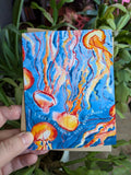 A greeting card with vibrant watercolour art of jellyfish with text on the front reading "I keep finding love everywhere I go."